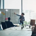 business-meeting-whiteboard-woman-speaker-with-presentation-office-planning-schedule-project-management-leadership-coaching-manager-hand-pointing-objectives-note-priority